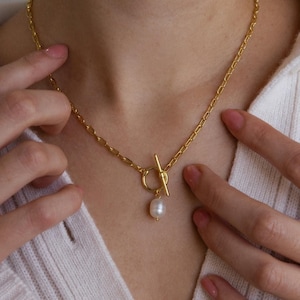 May include: A gold chain necklace with a toggle clasp and a single pearl pendant.