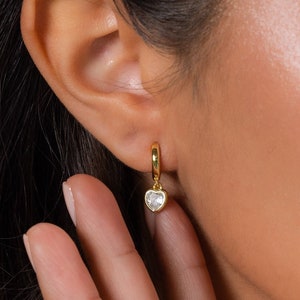 May include: Gold hoop earrings with a dangling heart-shaped crystal.