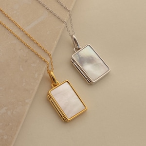 Könnte beinhalten: Zwei Halsketten mit rechteckigen Anhängern aus Perlmutt. Eine Halskette hat eine goldene Kette und die andere eine silberne Kette.