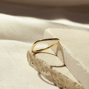 May include: A simple gold ring with a slightly oval shape, resting on two pieces of light beige stone.