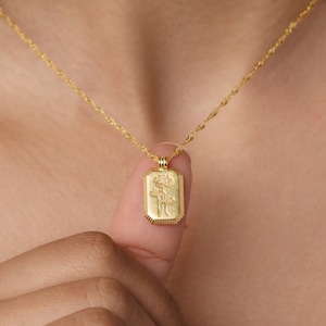 A gold twist chain has a rectangle pendant with an engraved flower on it. There are lines engraved along the outside of the charm and in the middle there is a daisy flower engraved design.