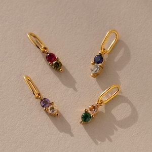 May include: Four gold charms with different coloured gemstones. Each charm has two gemstones, one larger than the other. The gemstones are red, green, blue, and purple.