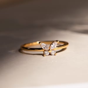 A close up of our Mariposa Butterfly Ring in 18K Gold finish placed on a white table with natural light coming in from the right side - featuring an about 5.5mm x 8mm CZ Diamond Butterfly Charm and an about 1.5mm Thin Ring Band.