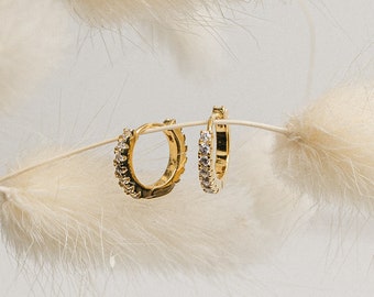 May include: A pair of gold hoop earrings with small clear stones set around the edge.