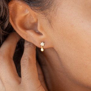 May include: A pair of gold earrings with a small star charm and a dangling pearl.