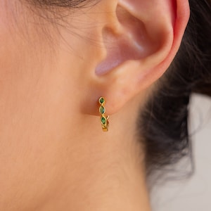 May include: Gold hoop earrings with small green gemstones. The earrings are small and delicate.
