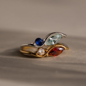 May include: A gold and silver ring with three gemstones: a blue sapphire, a light blue aquamarine, and a red garnet.