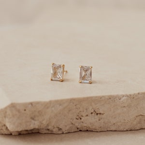 Puede incluir: Un par de pendientes de oro con piedras preciosas cuadradas transparentes.