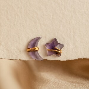 May include: A pair of earrings featuring a crescent moon and a star, both made of amethyst and wrapped in gold wire.