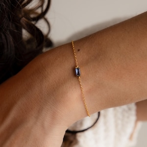 Puede incluir: Un delicado brazalete de cadena dorada con una sola piedra preciosa azul rectangular.