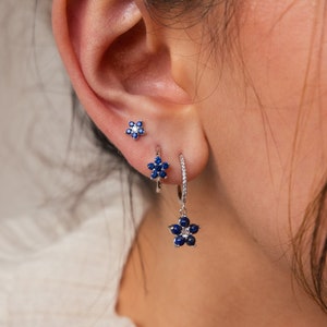 May include: A pair of silver earrings with blue flower charms. The earrings are made of sterling silver and feature a delicate flower design with blue gemstones. The earrings are perfect for adding a touch of elegance to any outfit.