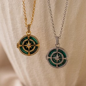 May include: Two gold and silver necklaces with green stone and diamond accents. The pendants are round and feature a compass design with a star in the center.