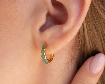 May include: Gold hoop earrings with small, round, green stones.