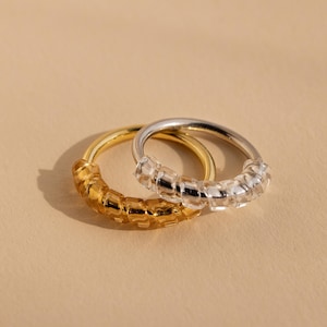 May include: Two rings, one gold and one silver, are stacked on top of each other. Both rings are made of small, square-shaped beads.