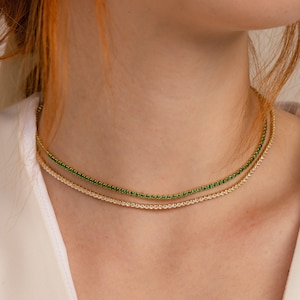 Puede incluir: Un collar de cadena de oro con dos filas de pequeñas piedras brillantes. La fila superior es verde y la fila inferior es transparente.