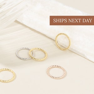 May include: Five gold, silver and rose gold twisted band rings on a light beige surface. The rings are all the same size and have a simple, elegant design.