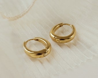 May include: Two gold hoop earrings on a white fabric background.