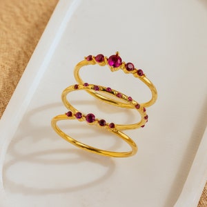 Op de afbeelding: Drie gouden ringen met roze edelstenen. De ringen zijn op elkaar gestapeld.