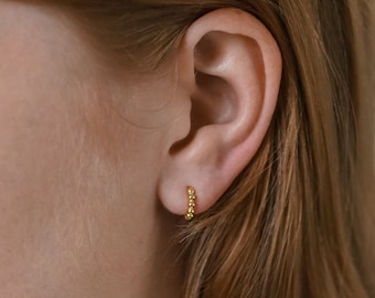 May include: A close-up of a person's ear wearing a small gold hoop earring made of tiny beads.
