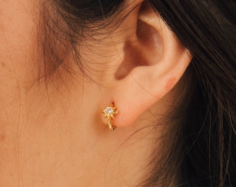 May include: Gold hoop earrings with a small star-shaped charm featuring a clear rhinestone in the center.