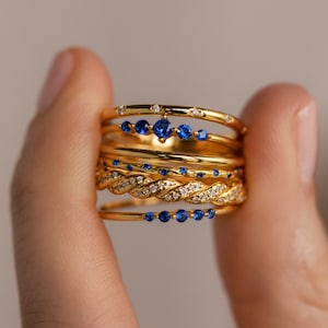 Model holds a stacked ring set consisting of dainty deep blue gemstone stacking rings and thin diamond bands.