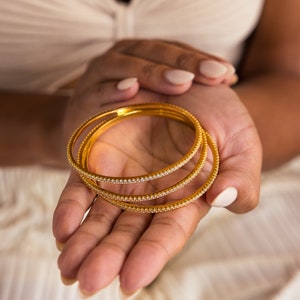 May include: Three gold bangles with a row of small clear stones around the edge.