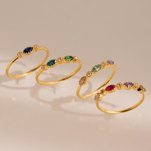 May include: Four gold rings with colourful marquise-shaped gemstones and small round clear stones. The rings are arranged in a row, with the blue ring on the left and the red ring on the right.