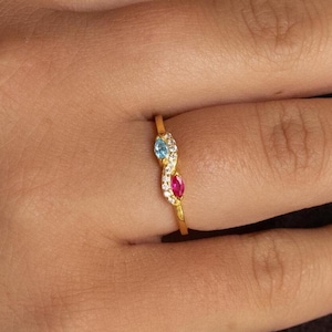 May include: A gold ring with a wave design and three gemstones. The gemstones are blue, red, and white.