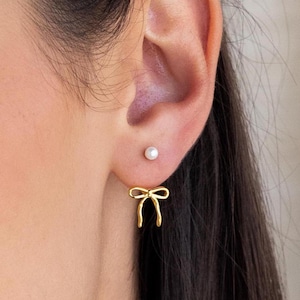 Könnte beinhalten: Ein Paar goldene Schleifenohrringe mit einem kleinen Perlenohrstecker im anderen Ohr.