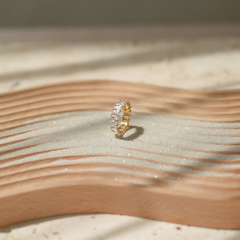 May include: A gold ring with a row of clear rectangular stones set in a band.