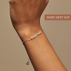 May include: A gold-colored bracelet with the word "mama" spelled out in sparkling, clear stones. The bracelet is delicate and has a small heart charm at the end of the chain. The text "SHIPS NEXT DAY" is in a brown rectangle.