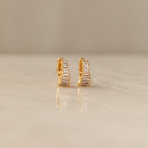 May include: A pair of gold hoop earrings with a row of clear cubic zirconia stones.
