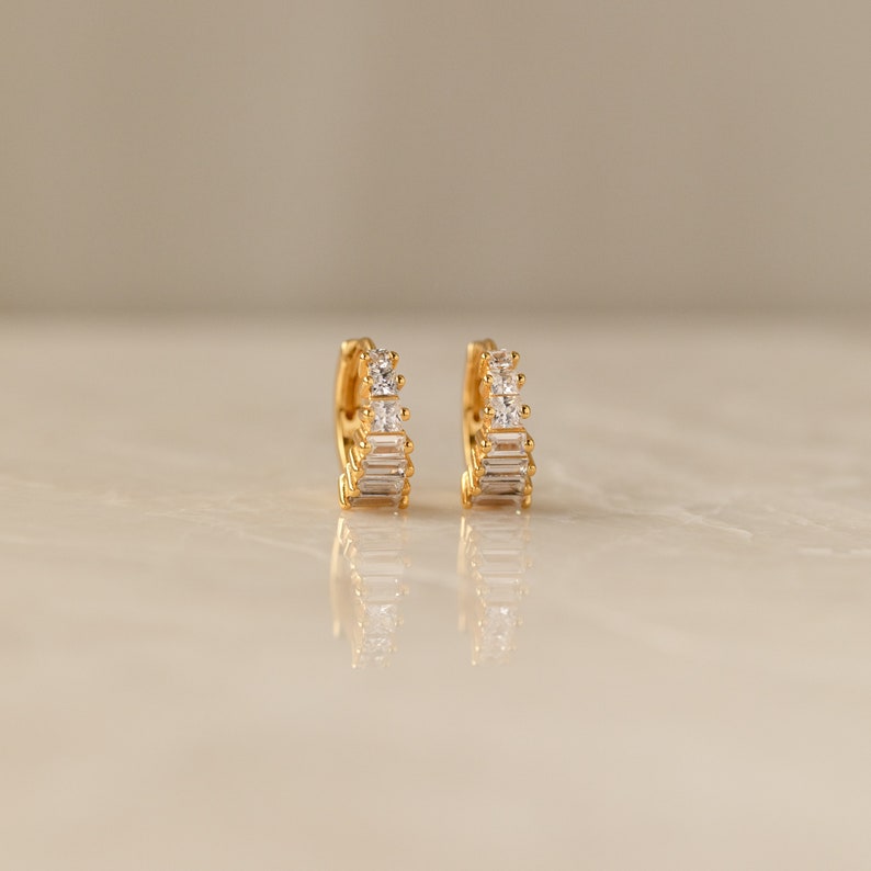 May include: A pair of gold hoop earrings with a row of clear cubic zirconia stones.