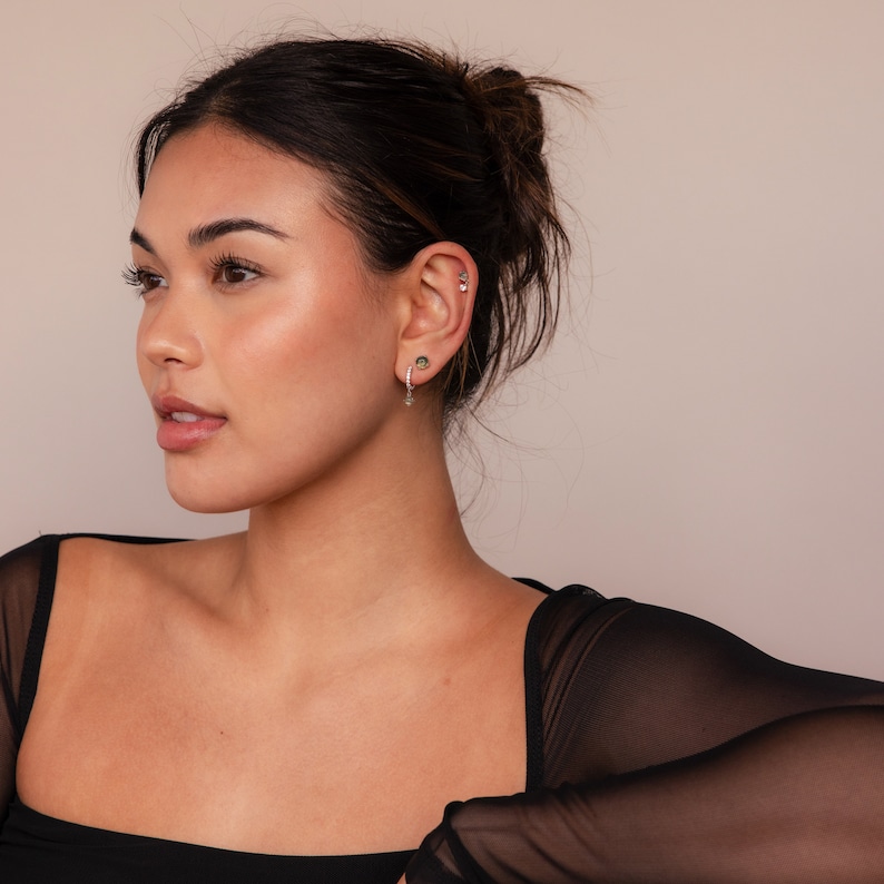 May include: A woman with dark brown hair wearing a black sheer top with a silver hoop earring with a small gemstone charm.