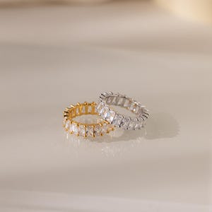 May include: Two eternity rings with a row of clear cubic zirconia stones. One ring is gold and the other is silver.