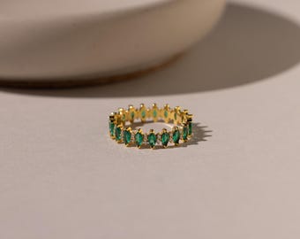 May include: A gold band ring featuring a continuous row of marquise-cut green stones alternating with small clear round stones. The metal setting is polished gold, and the design creates a repeating pattern of emerald-colored gems around the band.