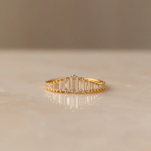 May include: A gold band ring with a row of clear baguette-shaped stones set in a graduated pattern.