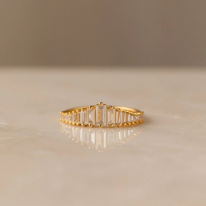 May include: A gold band ring with a row of clear baguette-shaped stones set in a graduated pattern.