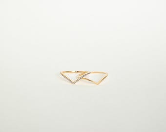 May include: Two gold-colored V-shaped rings. One ring is adorned with small, clear gemstones along the V-shape, while the other is a plain, polished gold. Both rings are set against a white background.