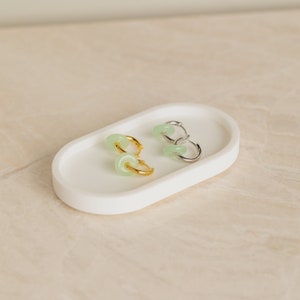 Peut inclure: Deux paires de cr&eacute;oles avec des accents de pierre verte. Une paire est en or et l'autre en argent. Les boucles d'oreilles sont pr&eacute;sent&eacute;es sur un plat ovale blanc.