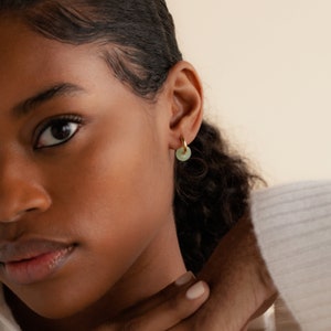 Peut inclure: Gros plan sur l'oreille d'une personne portant une boucle d'oreille en or avec un charme en pierre vert clair.