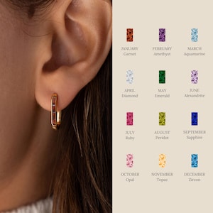 May include: Gold hoop earrings with a row of red gemstones. The earrings are shown on a model's ear. The image also includes a chart of birthstones for each month of the year.