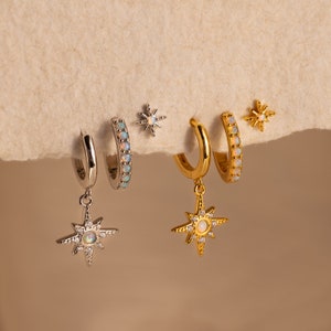May include: A set of three pairs of earrings featuring a starburst design with opal accents. The earrings are available in both gold and silver.