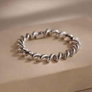 May include: A silver bracelet with a spiral design. The polished metal bracelet has a clasp closure. The design is a continuous, twisting pattern, creating a modern and elegant look. The bracelet is displayed on a neutral background.