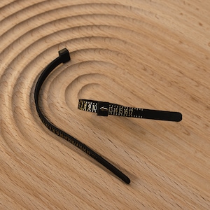 May include: Black flexible measuring tape with gold markings. The tape is marked with numbers from 7 to 17.