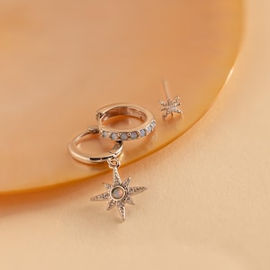 May include: A set of silver earrings featuring a star charm with an opal stone and a hoop earring with a row of white stones.