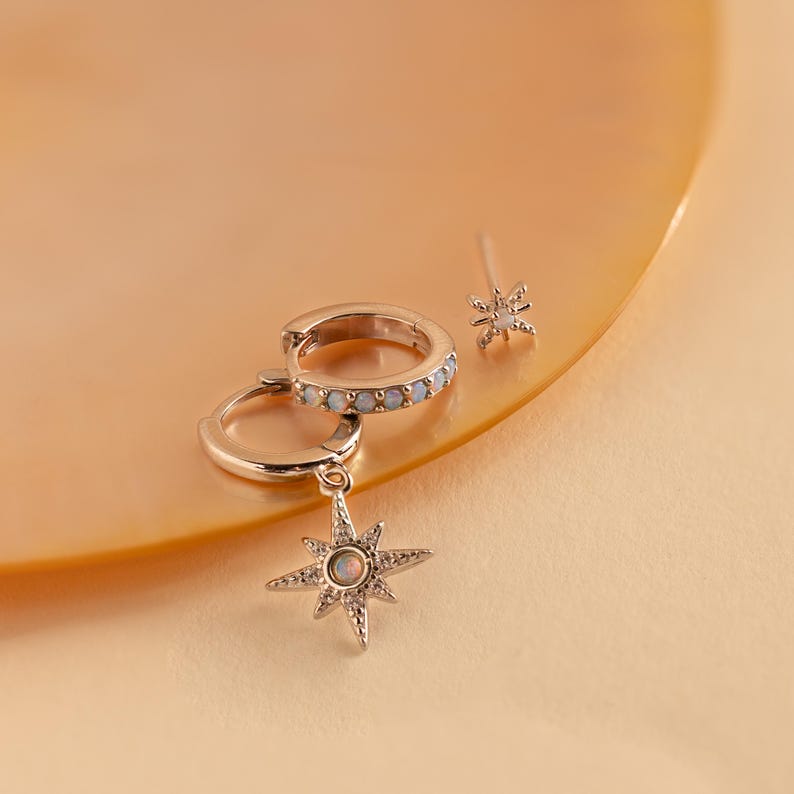 May include: A set of silver earrings featuring a star charm with an opal stone and a hoop earring with a row of white stones.