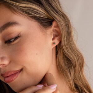 K&ouml;nnte beinhalten: Nahaufnahme eines Frauenohrs mit einem kleinen gr&uuml;nen Edelstein-Ohrring. Der Ohrring ist ein schlichter Stecker.