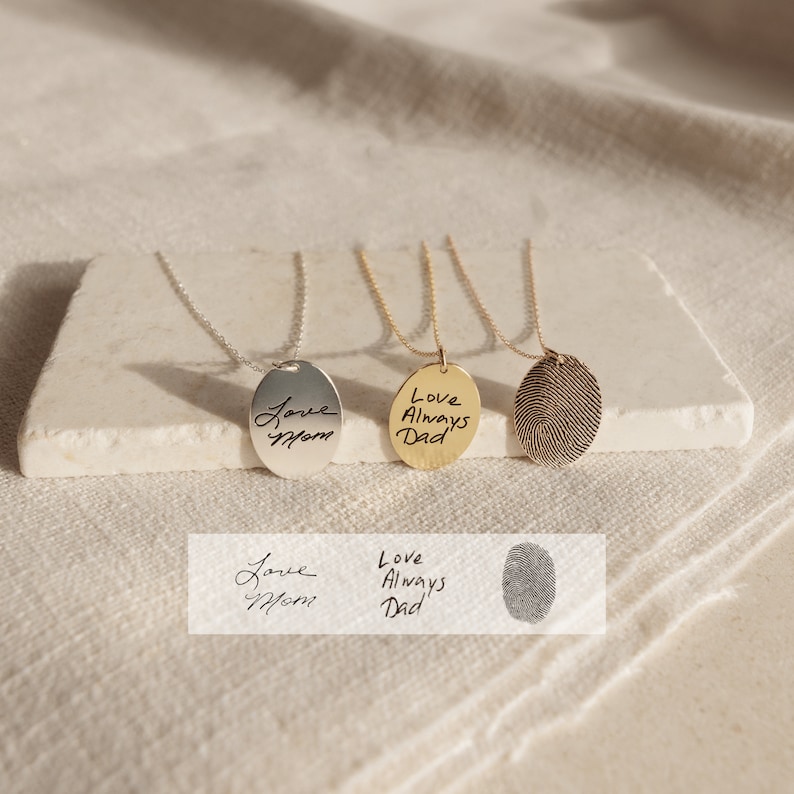 May include: Three silver necklaces with oval pendants. The pendants feature handwritten text, "Love Mom", "Love Always Dad", and a fingerprint design.
