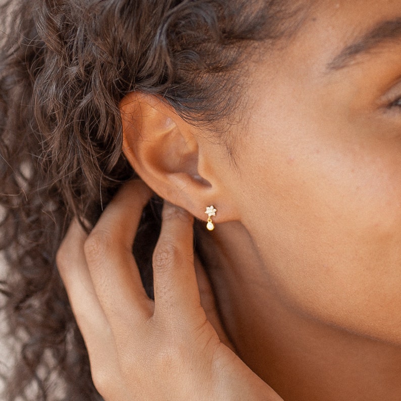 May include: A pair of gold earrings with a small star charm and a dangling pearl.